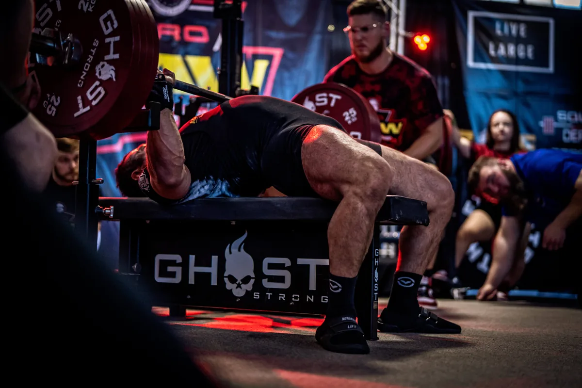 Lifter bench pressing with spotters at a powerlifting meet
